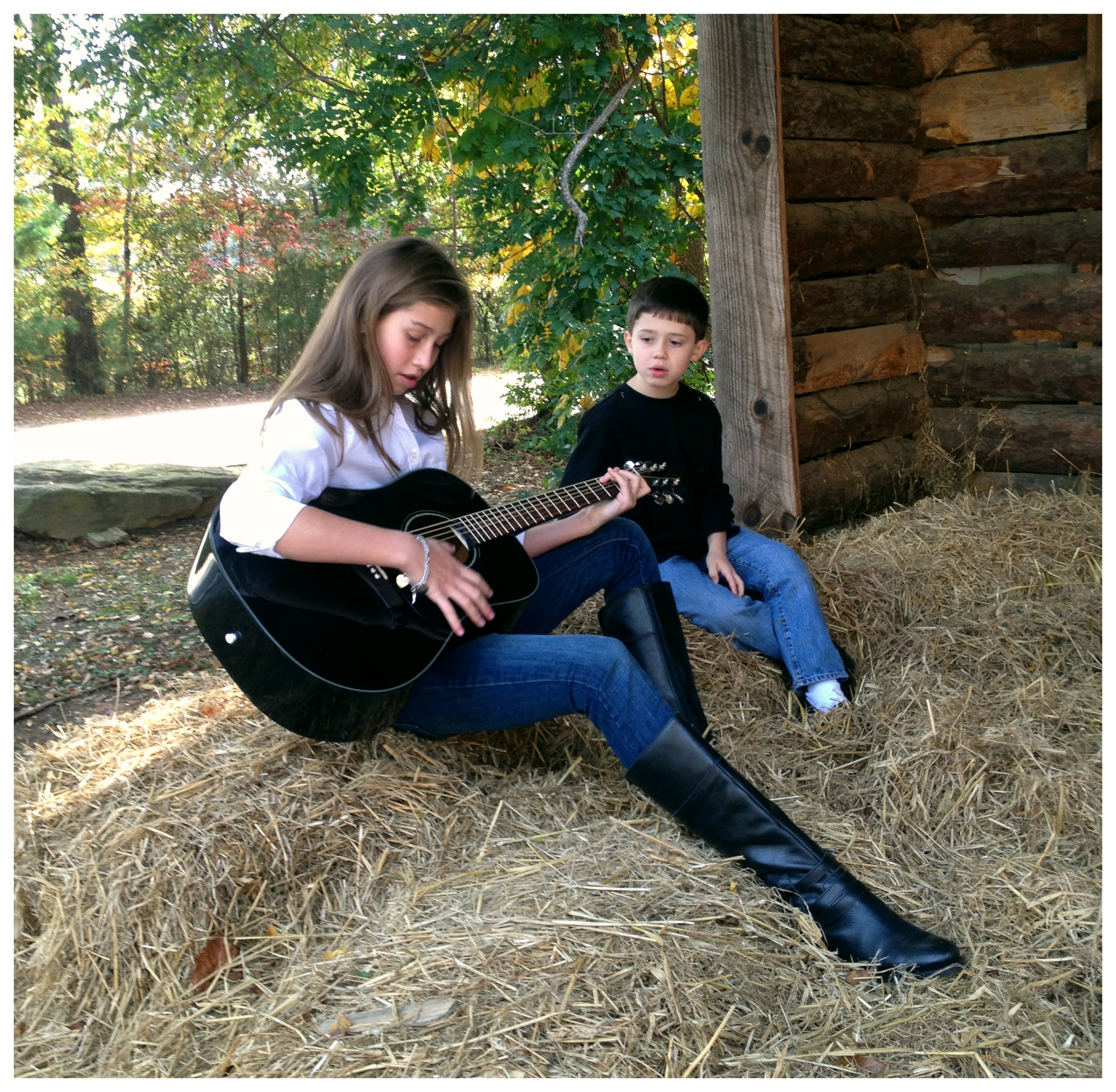 Big sister playing guitar for her little brother in a barn