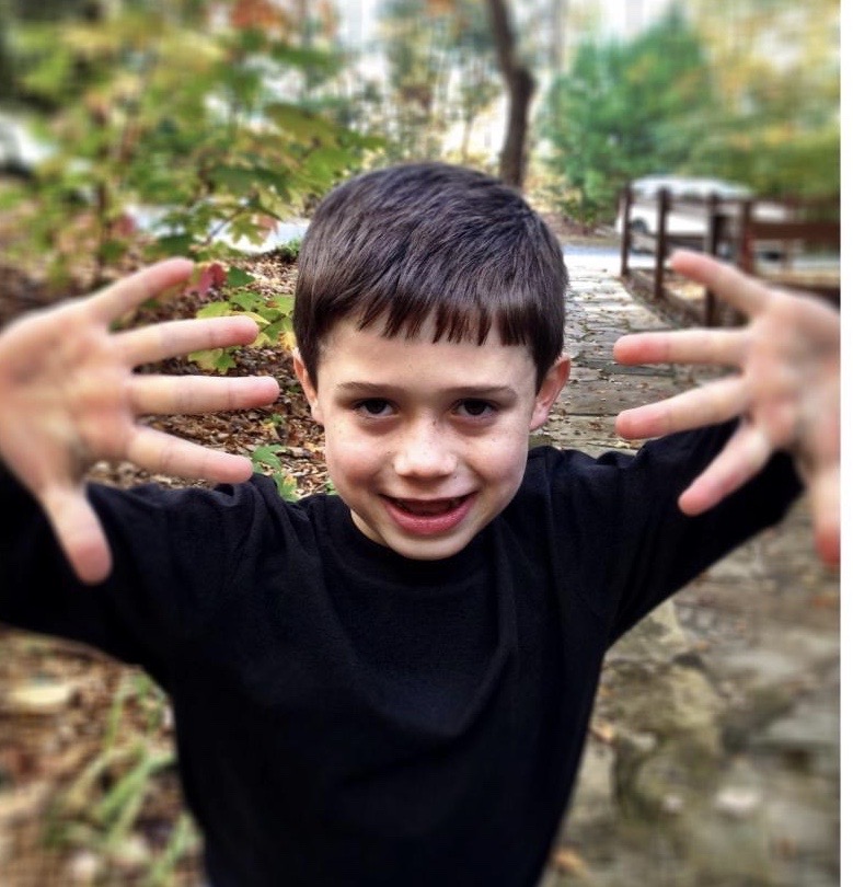 Young boy reaching toward the camera on a fall trail